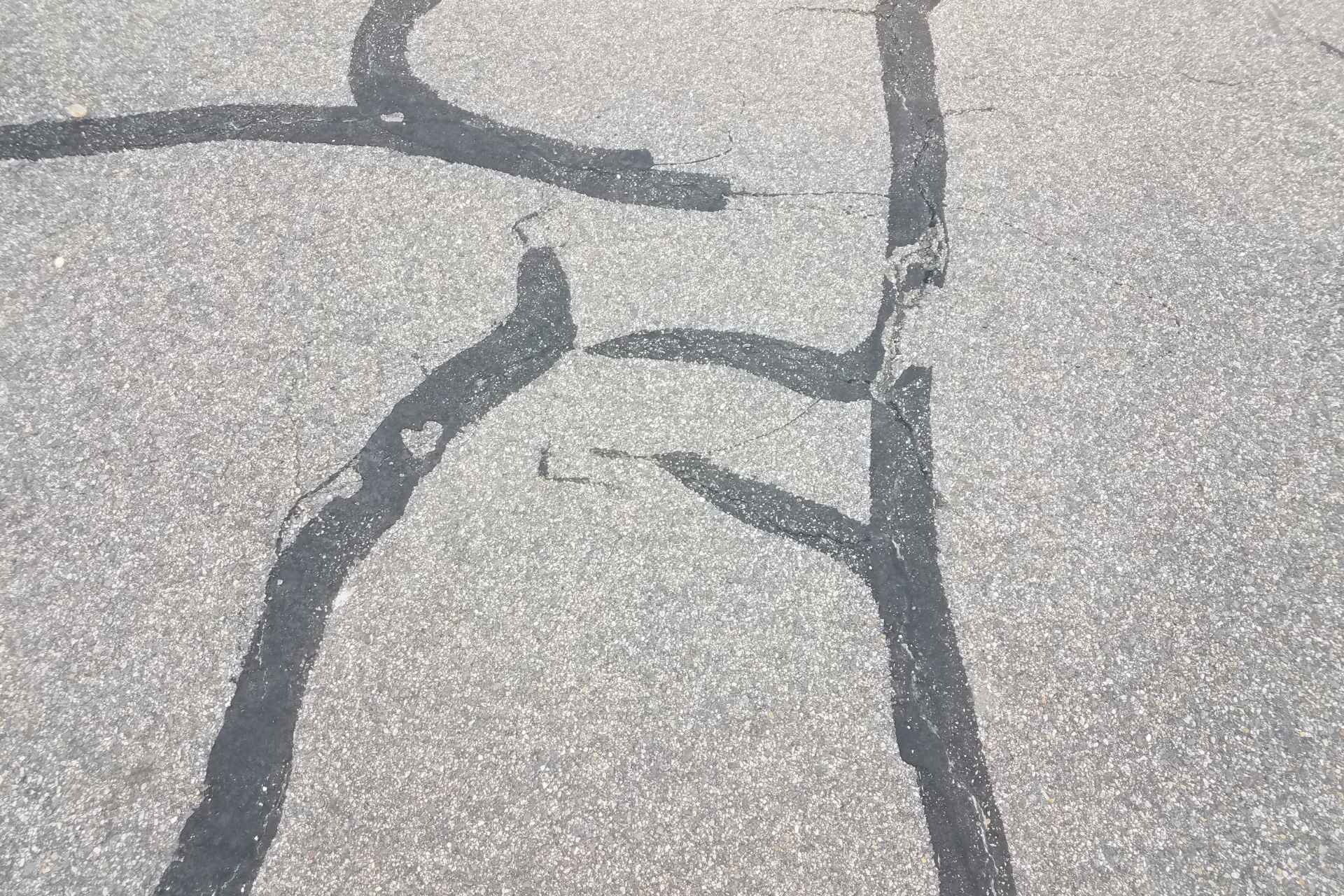 Black asphalt surface with filled-in cracks using crack filler.